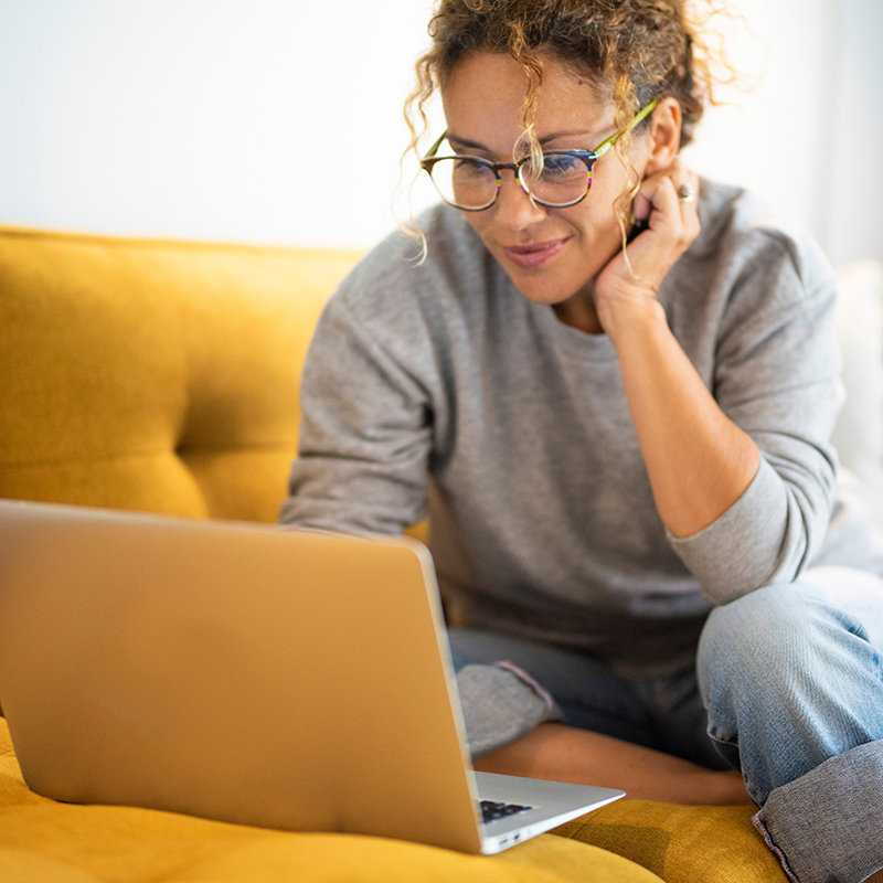 Vrouw zit op gele zetel met laptop